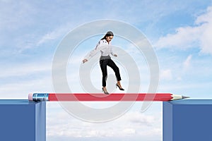 Attractive european female crossing pencil bridge on sky background. Career problem and gap concept