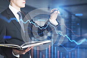 Attractive young european man using abstract falling downword forex chart interface on blurry office interior background.