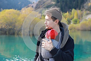 Attractive young father with her infant baby in sling outdoor. Babywearing concept