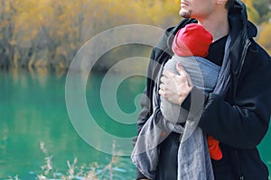 Attractive young father with her infant baby in sling outdoor. Man is carrying her child and travel in autumn mountain