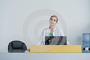 Attractive young female doctor leaning on the clinic reception desk, medical staff and healthcare concept.