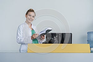 Attractive young female doctor leaning on the clinic reception desk, medical staff and healthcare concept.