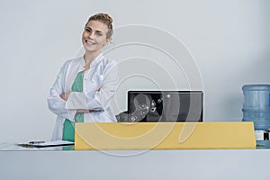 Attractive young female doctor leaning on the clinic reception desk, medical staff and healthcare concept.