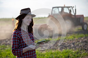 Attractive young female farmer standing using tablet with tractor in background