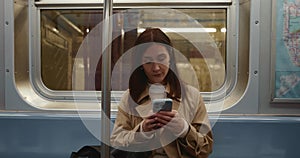 Attractive young female looking around subway carriage and texting using smartphone