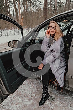 Attractive young female looks out the car window waiting for a trip and smile. Winter travel. Woman sitting in the car