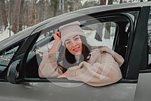 Attractive young female looks out the car window waiting for a trip and smile. Winter travel. Woman sitting in the car