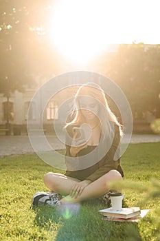 Attractive young female student using her smartphone in the college park on the lawn in the sunlight. Beautiful happy student girl