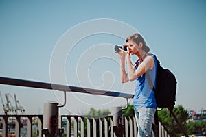 Attractive young female tourist with backpack and camera is exploring Hamburg city. Woman is making photo on retro