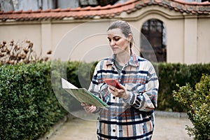 Attractive young female tourist is exploring city. Happy woman holding a paper map and phone on city street. Traveling