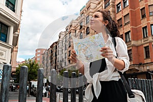 Attractive young female tourist exploring european city. Woman with map in hands searching right direction on map