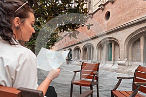 Attractive young female tourist exploring european city. Woman with map in hands searching right direction on map