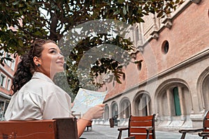 Attractive young female tourist exploring european city. Woman with map in hands searching right direction on map