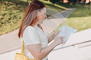 Attractive young female tourist is exploring new city. Happy redhead Woman with map in hands