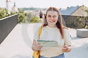 Attractive young female tourist is exploring new city. Happy redhead Woman with map in hands