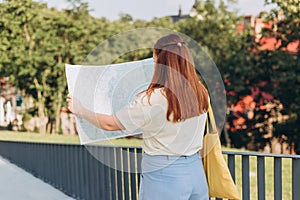 Attractive young female tourist is exploring new city. Happy redhead Woman with map in hands