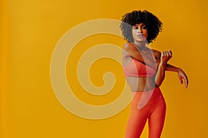 attractive young fit woman in sportswear stretching isolated on orange background