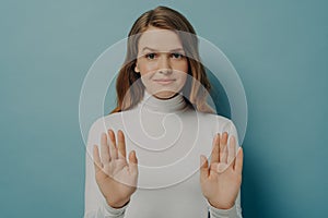 Attractive young focused woman showing stop gesture, saying no, isolated over blue studio background