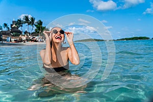 Attractive young girl is bathing on the beach in clear turquoise sea water and laughing merrily. Portrait of a young girl in the