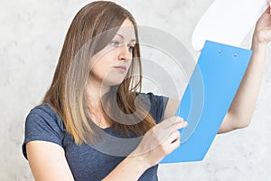 Attractive young girl with clipboard folder with blank white sheet of paper. Modern businesswoman looks at a report on paper. Lady