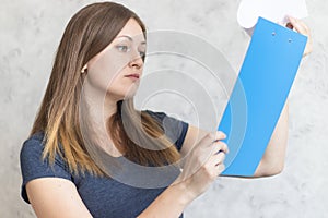 Attractive young girl with clipboard folder with blank white sheet of paper. Modern businesswoman looks at a report on paper. Lady