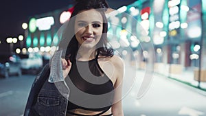 Attractive young girl comes to the camera, and smiles happily, shyly touches her hair. Fashionable, hot outfit. Urban