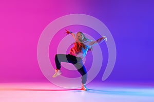 Attractive young girl dancing hip-hop isolated on gradient pink purple neon studio background