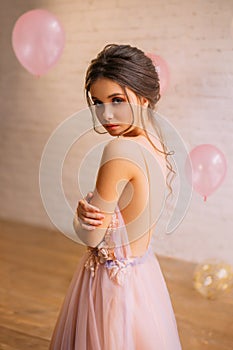 Attractive young girl with dark hair in a gorgeous hairstyle, dressed in a long gentle pink with a purple dress with an