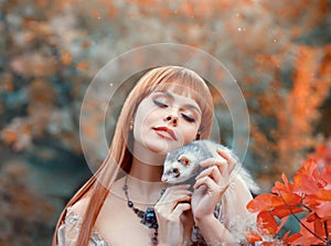 Attractive young girl with fiery red straight hair plays with her pet, elf princess plays animal fairy with wild ferret