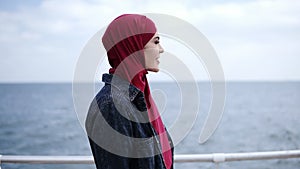 Attractive young girl with hijab on her head is walking supposedly near the sea side with seagulls flying on the