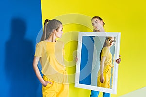 Attractive young girl holding mirror for her friend on blue