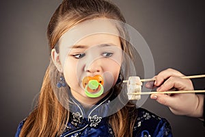 Attractive young girl with pacifier in mouth looking sushi rolls