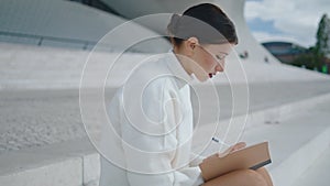 Girl student making notes in notebook sitting stairs closeup. Lady writing diary