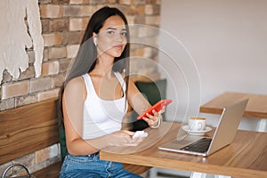 Attractive young girl use wirreless headphones and workin on her laptop. Woman in white t-shirt and denim. Student study