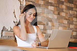 Attractive young girl use wirreless headphones and workin on her laptop. Woman in white t-shirt and denim. Student study