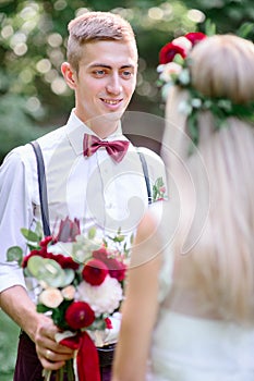 Attractive young groom in blue braces stands before bride