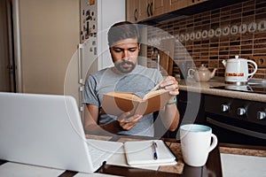 Attractive young hipster man focused reading book at home office