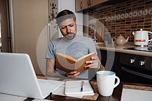 Attractive young hipster man focused reading book at home office