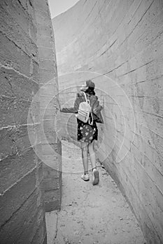 Attractive young woman stands between concrete walls. Caucasian girl in casual jeans and flower dress looks up.