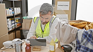 Attractive young hispanic man with grey hair, volunteering at a charity center, passionately works online via touchpad while