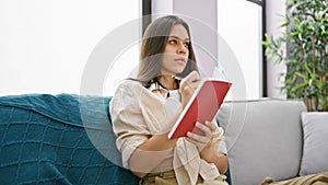 Attractive young hispanic woman savors tranquil moments of comfort, lounging on her sofa at home