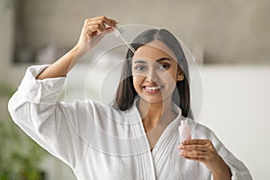 Attractive young indian woman applying moisturizing serum onto her face