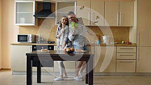 Attractive young joyful couple have fun dancing and singing while cooking in the kitchen at home