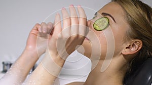 Attractive young lady applying cucumber slices in bath, natural skincare product