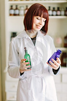 Attractive young lady pharmacist with a lovely smile standing working and holding glass vintage bottles of medicines in