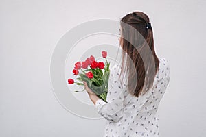 Attractive young lady in white shirt hold a bouquet of red flowers. White background. Back view