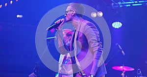 Attractive young male singer in glasses performing with band at live music event. Portrait handsome musician singing