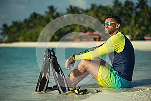 attractive young man on the beach with snorkeling equipment observes the coral world, free diver in the sea