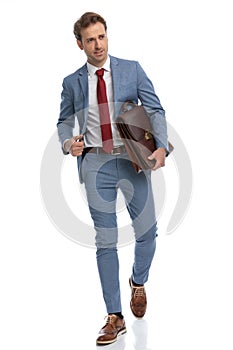 Attractive young man in blue suit looking to side and holding briefcase