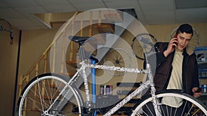 Attractive young man cheerful mechanic is talking on mobile phone and assembling bicycle handle-bar. People, maintenance